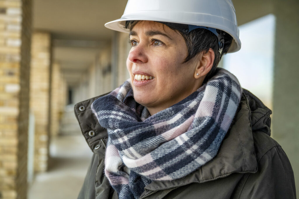 Vorsicht beim Hausbau im Winter – Temperatur mit mobiler Heizzentrale sichern Hausbau Helden Bauleiterin mit Helm und Schal bei winterlichen Temperaturen