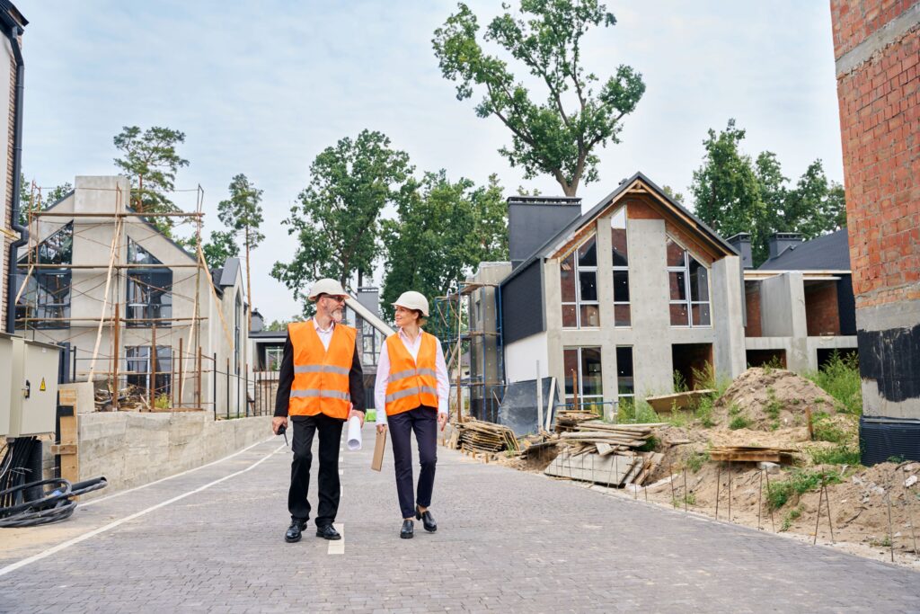Ein Bauarbeiter und eine Bauarbeiterin laufen gemeinsam über eine Baustelle mit Neubauten.
