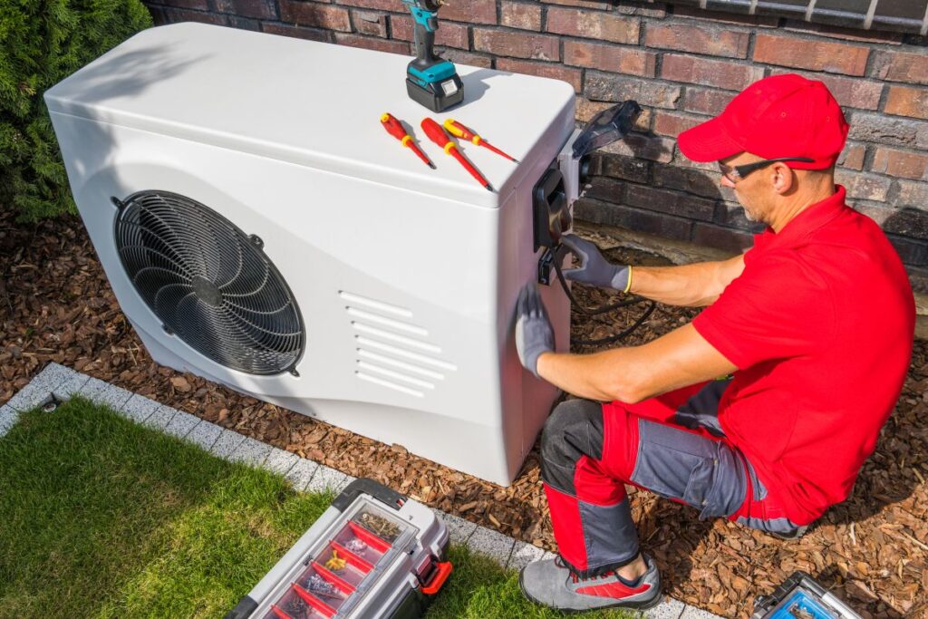 Professioneller HLK-Techniker mittleren Alters in roter Uniform, der moderne Wärmepumpeneinheit repariert.
