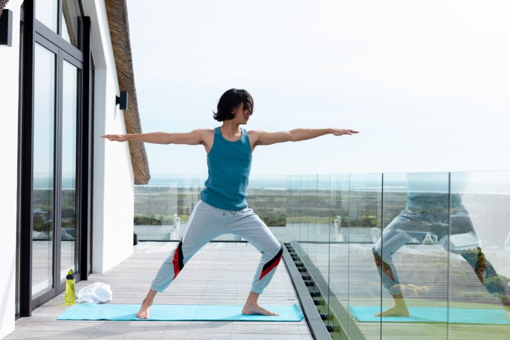 Ideen für die Balkongestaltung und die optimale Nutzung Hausbau Helden Glücklicher biracialer Mann, der Yoga macht und sich auf dem Balkon dehnt. Alleinstehende Zeit zu Hause verbringen, häusliches Leben und Lifestyle-Konzept.