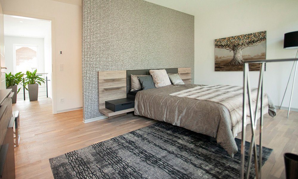 Musterhaus Bad Vilbel - Ein Schlafzimmer mit einem Bett und einem Stuhl in einem Raum - Interior Design Services