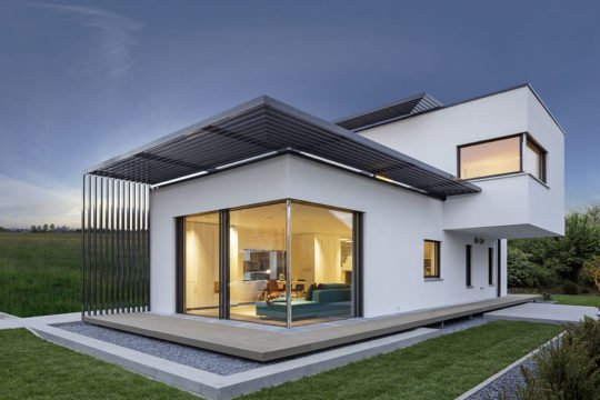 Musterhaus Fine - Ein großes Backsteingebäude mit Gras vor einem Haus - Haus