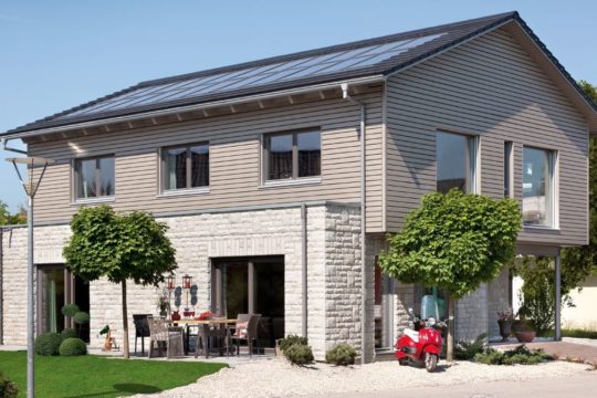 Energieplus Haus Poing - Ein großes Backsteingebäude mit Gras vor einem Haus - SchwörerHaus KG Musterhaus Poing