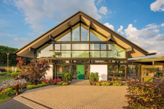 HUF HAUS Musterhaus Köln - Ein großes Backsteingebäude mit Gras vor einem Haus - HUF HAUS Musterhaus Köln