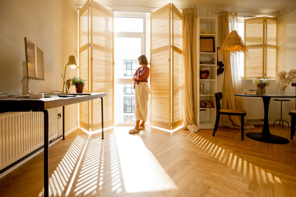 Sonnenlicht: Eigenschaften und deren Wirkung auf dein Haus Hausbau Helden Eine Frau steht am sonnendurchfluteten Fenster und blickt hinaus.