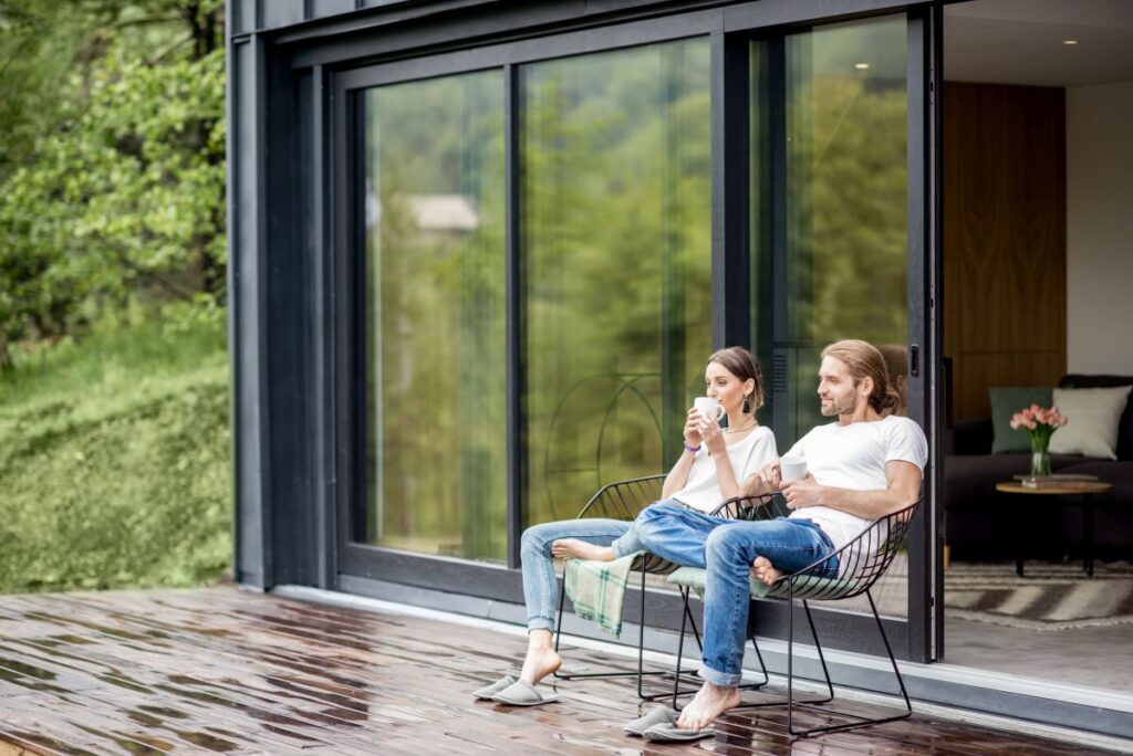 6 Tipps zur Absicherung für Hausbesitzer Hausbau Helden Junges Paar sitzt auf der Terrasse vor ihrem Haus