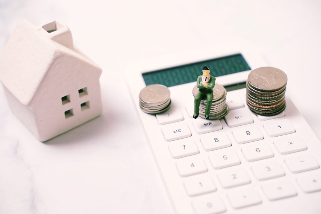 Wichtige Nebenkosten von Hausbesitzern Hausbau Helden Miniatur-Geschäftsleute sitzen auf einem Stapel Münzen auf Taschenrechner mit Haus-, Finanz- und Immobilienkonzept