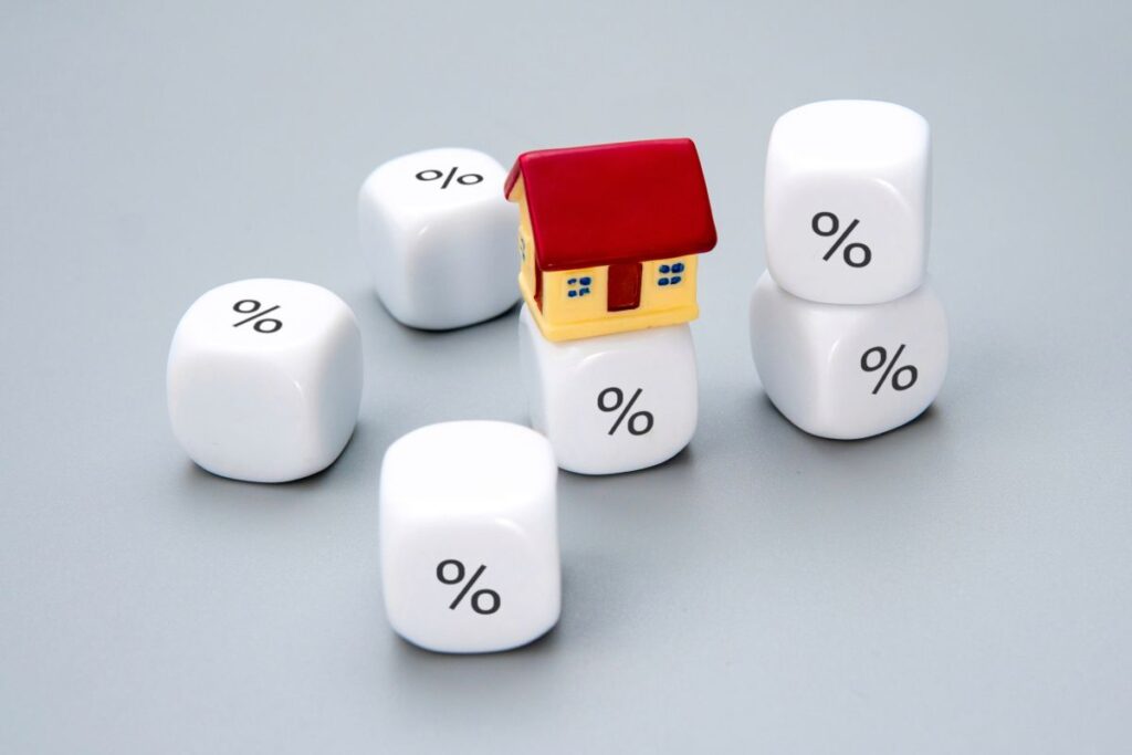 Bauzinsen im Wandel - Strategien für volatile Zeiten Hausbau Helden Ein kleines Haus, umgeben von Würfeln mit Prozentzeichen.