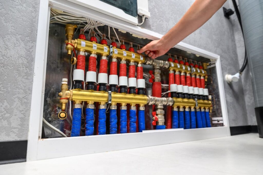 Moderner Elektroboiler im Haus. Verteiler für Fußbodenheizungen. Ein Mann richtet das System ein, Nahaufnahme einer Hand