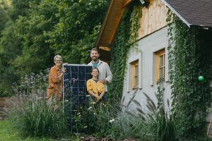 Solardach 2024: Die Kraft der Sonne nutzen Hausbau Helden Eine dreiköpfige Familie steht im Garten ihres Haus und hält ein Solarpanel in der Hand